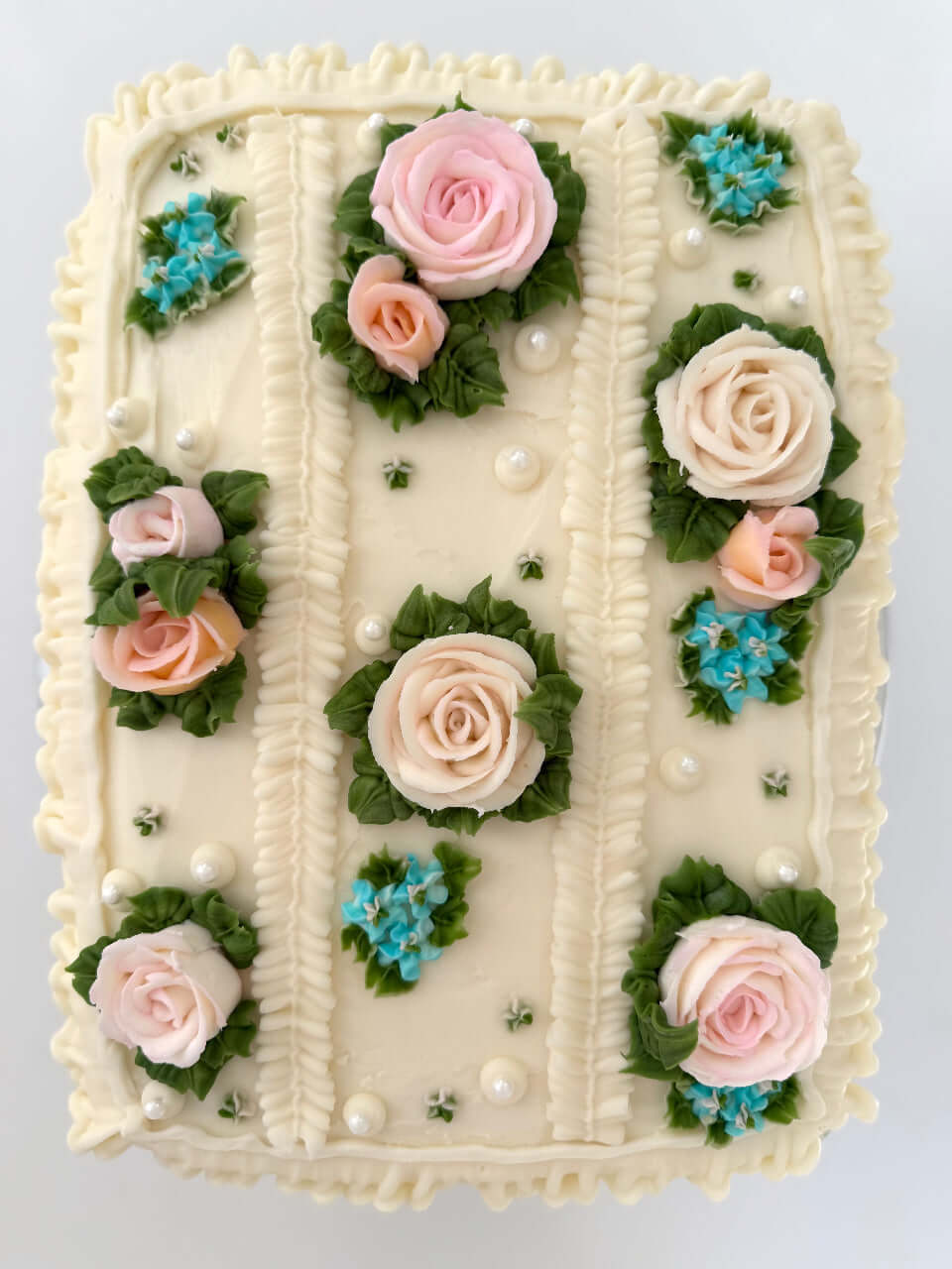 Decorative cake with pink and white roses, green leaves, and blue flowers on a white background