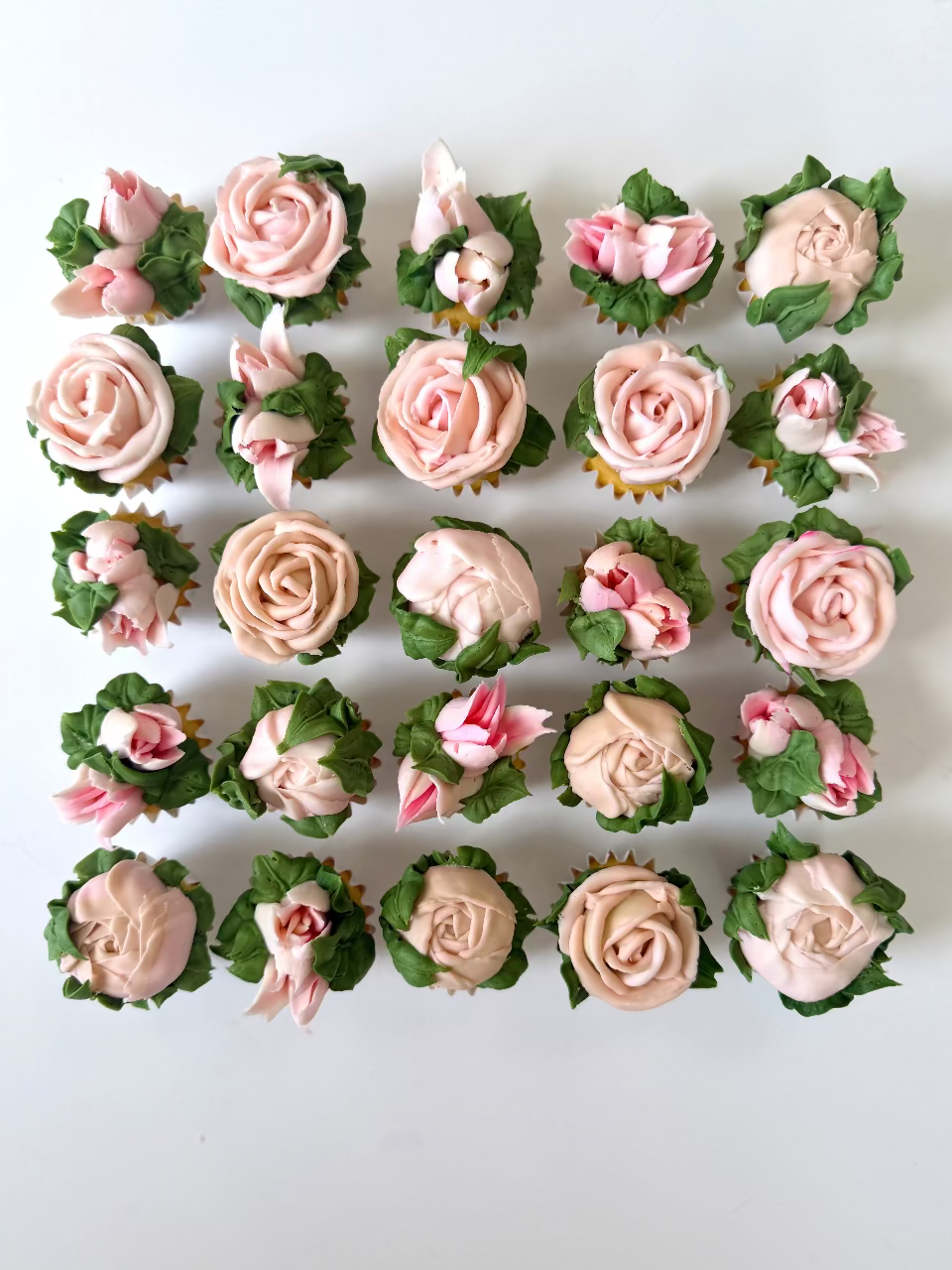 Decorative cupcakes with pink and green icing arranged in a grid on a white background